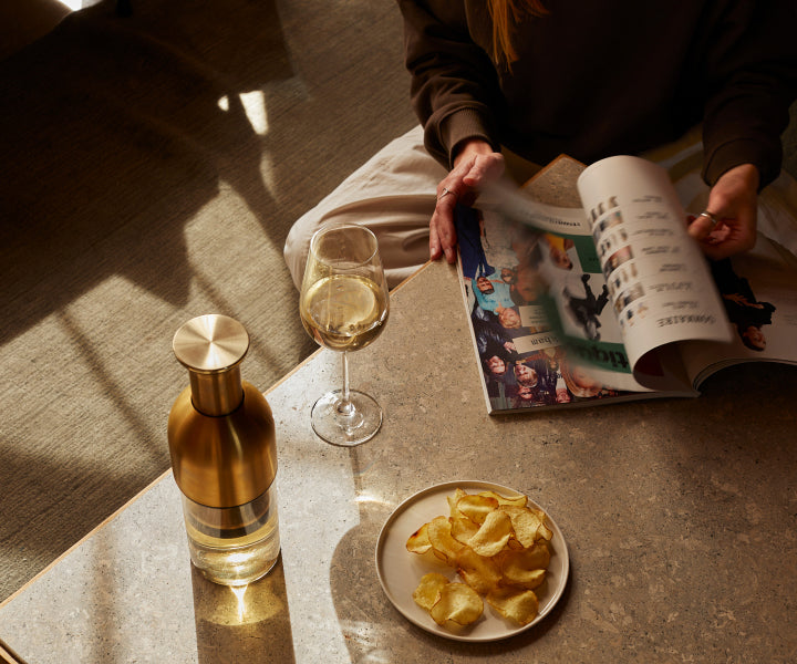 Woman reading a magazine with a plate of crisps and a glass of white wine and eto wine decanter