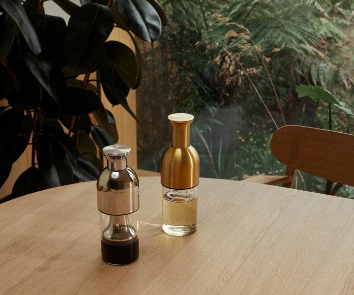 A stainless mirror eto wine decanter containing red wine beside a brass eto wine decanter with white wine on a wooden table